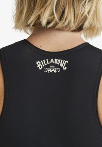 Parte superior de traje de neopreno negro con costuras cosidas. Cuenta con el logo blanco "Billabong" y el texto "desde 1973" en la parte superior de la espalda. Textura suave.