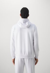 Felpa bianca con cappuccio realizzata in tessuto morbido. Presenta maniche lunghe, polsini a righe e un orlo in vita, con un design semplice e pulito.