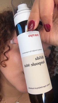 Schwarze, zylindrische Sprühflasche mit einem weißen Etikett. Der Text umfasst "Bitiqa Ample Mist" und "Sichtbar altersbestimmend und feuchtigkeitsspendend." Durchsichtige obere Kappe.