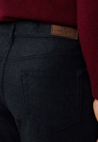 Pantalons en denim foncé à la texture lisse, avec une étiquette en cuir portant la mention "HACKETT" sur la taille et deux poches arrière.