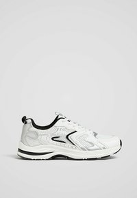 Baskets blanches de sport avec des détails noirs et gris, design à lacets, semelle texturée et languette au talon, vues de côté sur fond gris.