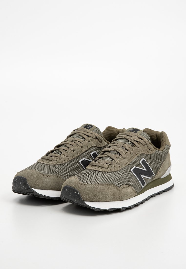 Sneaker verde oliva in materiale mesh e suede, con lacci piatti, logo "N" nero in evidenza, suola testurizzata con accenti bianchi e neri.
