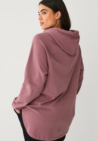 Hoodie in stoffige rozenkleur, met een ontspannen pasvorm, lange mouwen en zijzakken. Zacht, gestructureerd materiaal met een gladde afwerking.