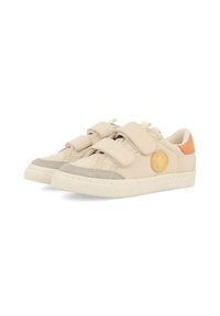 Zapatillas de lona beige con correas de velcro, acentos de ante gris, detalle de logo redondo y una etiqueta en el talón de color naranja contrastante. Suela de goma.