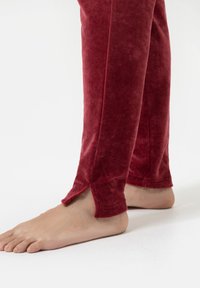 Rode fluweel loungesweaters met een zachte textuur, voorzien van zijslitsen bij de enkels. De broeken hebben een getailleerd ontwerp en geen zichtbare hardware.