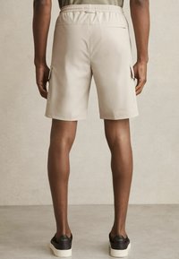 Beige shorts med elastisk talje og sidelommer, lavet af glat stof. Har en skræddersyet pasform og en design, der går til midten af låret.