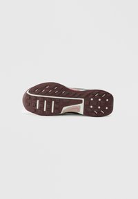 Semelle de chaussure de trail avec des rainures profondes et texturées, en caoutchouc rouge foncé, et une semelle intermédiaire de couleur claire avec un motif en maille et des ports de ventilation.