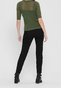 Oliwkowy sweter z krótkimi rękawami, dzianinowy, z wzorzystą fakturą; połączony z dopasowanymi czarnymi spodniami i botkami za kostkę.