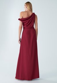 Burgundia ülikleit, millel on avatud õlad, drapeeritud kangas, põrandani ulatuv disain, siidine tekstuur ja peened voltimised vööl ning seljal.