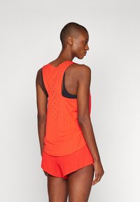 Rotes sportliches Tanktop mit Mesh-Details, kombiniert mit passenden roten Shorts. Der Stoff scheint leicht und strukturiert zu sein, geeignet für sportliche Aktivitäten.