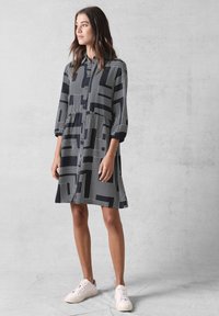 Abito button-down bianco e nero con motivi geometrici a linee, maniche a tre quarti e vestibilità comoda. Orlo svasato sopra il ginocchio.