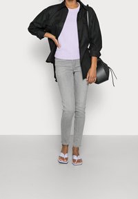 Czarna overshirt nałożona na jasnopurpurowy sweter z dzianiny, szare dopasowane jeansy i purpurowe klapki. Czarna siatkowa torba na ramię.