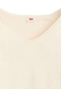 T-shirt en coton beige clair avec un col en V et une texture douce. Présente un motif côtelé subtil et une étiquette indiquant la marque et la taille au niveau du cou.