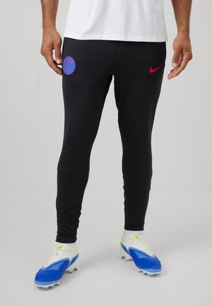 Črne slim-fit atletske hlače z modrim krožnim logotipom Pariza in rdečim Nikeovim žigom, v kombinaciji z belimi in modrimi nogometnimi krami.