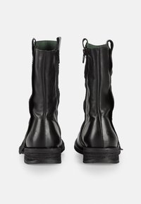 Botas de cuero negras hasta el tobillo con una textura suave, cremalleras laterales y un tacón apilado. Vista trasera con un minimalismo en los detalles y costuras decorativas.