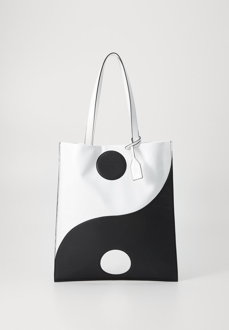 Sac fourre-tout noir et blanc avec un motif yin-yang, comportant un accent noir circulaire et une étiquette suspendue. Fabriqué en matériau synthétique lisse.