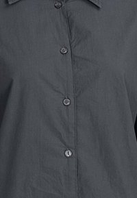 Chemise gris foncé à col avec boutons visibles sur le devant et texture subtile du tissu.