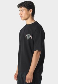 Sort bomulds t-shirt med rund halsudskæring, korte ærmer og forstærket broderi med et blomsterdesign samt ternede accenter.