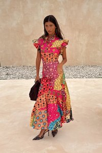 Kleurrijke patchwork jurk met gerimpelde mouwen, featuring diverse patronen in roze, geel, oranje en blauw. Model houdt een donkere handtas vast.