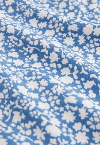 Tissu bleu avec un motif floral blanc, présentant des fleurs et des feuilles petites à moyennes, texture douce et apparence texturée, drapé en plis.