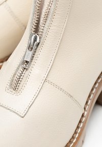 Acercamiento de una bota de cuero beige que presenta una cremallera plateada YKK y una costura detallada a lo largo de la parte superior y la suela.