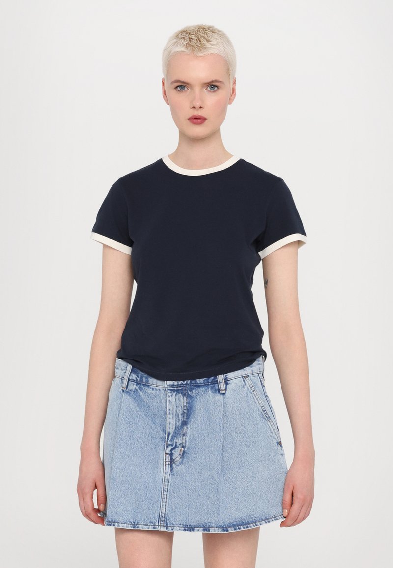 Marinefarbendes Baumwoll-T-Shirt mit cremefarbener Rundhalsausschnitt- und Ärmelschneide, kombiniert mit einem hellblauen Jeansrock mit tailliertem Bund und Taschen.