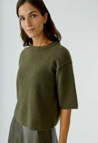 Olivgrüner Kurzarmpullover aus weichem, strukturiertem Material mit einem runden Ausschnitt und einer lockeren Passform, kombiniert mit einem glatten Rock.