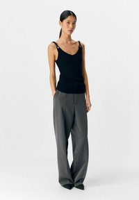 Top de tirantes negro acanalado con escote en V, con tirantes en forma de cadena; combinado con pantalones grises anchos y con pliegues que aportan una silueta relajada.