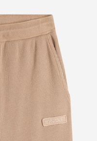 Jogger in tessuto a coste beige con vita elasticizzata e tasche laterali. Presenta un piccolo logo ricamato sul davanti.