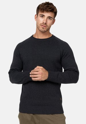 Jersey de punto gris oscuro con cuello redondo y puños acanalados. Presenta una tela texturizada y un pequeño logotipo cerca del dobladillo.