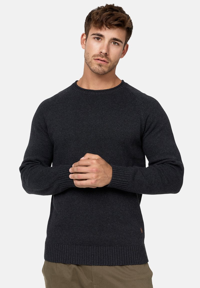 Jersey de punto gris oscuro con cuello redondo y puños acanalados. Presenta una tela texturizada y un pequeño logotipo cerca del dobladillo.