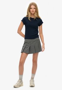Marineblauw aansluitend T-shirt met korte mouwen, gecombineerd met een grijs gestreepte minirok. Model draagt beige sneakers en grijs gestreepte sokken. Eenvoudige, sportieve look.