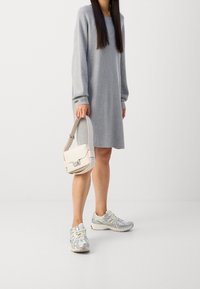 Robe-pull gris clair à manches longues, associée à des baskets blanches et un petit sac à main crème avec une fermeture argentée.