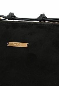 Borsa a mano in suede nera con una finitura testurizzata, caratterizzata da una targhetta metallica dorata del marchio e dettagli in pelle annodata sul manico. Chiusura con zip nella parte superiore.