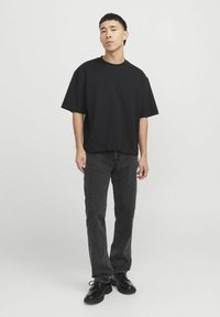 Juodas per didelis T-shirt iš minkštos medvilnės, derinamas su tamsiai pilkais tiesiais džinsais. Juodi bateliai su raišteliais užbaigia šį derinį. Paprastas ir modernus dizainas.