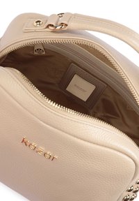 Beżowa skórzana torebka o zwartej formie, z elementami w kolorze złotym, zamkiem błyskawicznym i detalem z logo wewnątrz. Gładka tekstura z widocznym wzorem podszewki.
