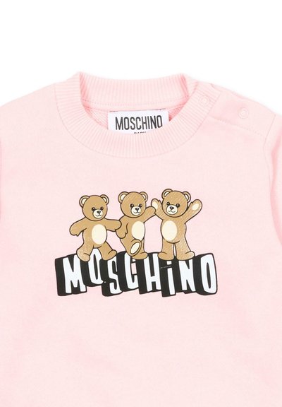 Camiseta de bebé en rosa claro con tres ositos bailarines sobre el nombre de la marca MOSCHINO en letras negras y blancas.