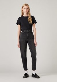 Black short-sleeve T-shirt paired with high-waisted black jeans. Model wears white socks and black loafers. Simple, minimalist style.