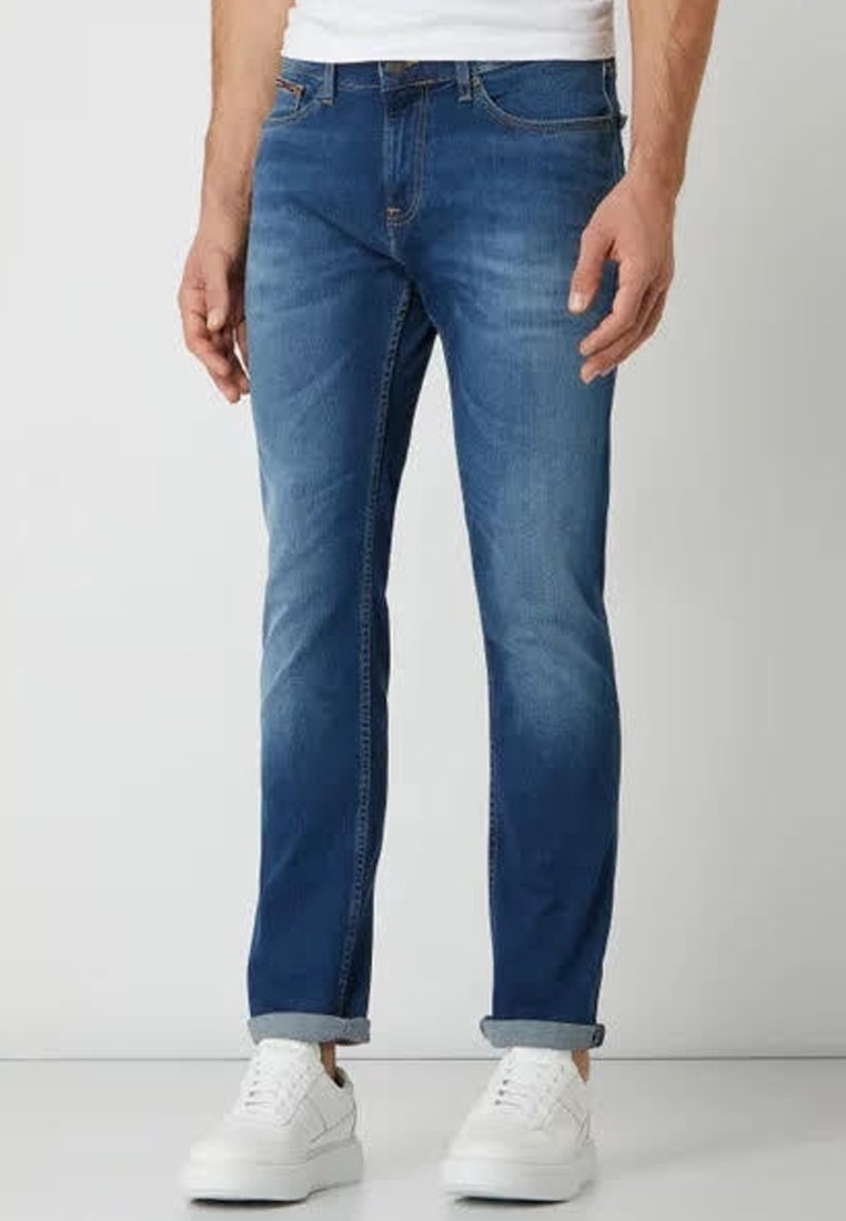 Blue denim jeans with a straight cut, faded finish, and rolled cuffs. Features five pockets and stitched seams. Worn with white sneakers.