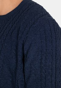 Maglione lavorato a maglia blu navy con un motivo a treccia testurizzato e collo a costine, che presenta dettagli di cucitura intricati e un tessuto morbido.