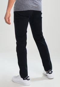 Svarta bomullsbukser med rak skärning, slät textur och elastisk midja, i kombination med vita sneakers med marinblå detaljer.