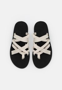 Zwarte sandalen met kruislings beige stoffen banden en een zachte voetbed. Het ontwerp is minimalistisch met een platte zool en open teenstijl.