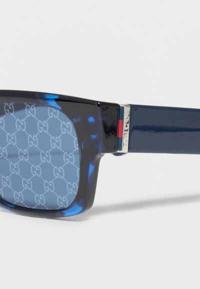 Μπλε ορθογώνια γυαλιά ηλίου με μοτίβο χελωνόσαρκας, διάκοσμο GG στους φακούς και ασημί, κόκκινες και πράσινες λεπτομέρειες στον βραχίονα του σκελετού.