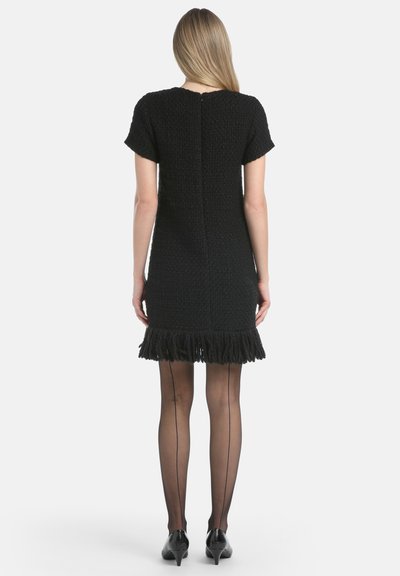Abito nero a maniche corte con tessuto texture, orlo frangiato e zip sul retro. Abbinato a collant neri trasparenti e scarpe nere con punta.
