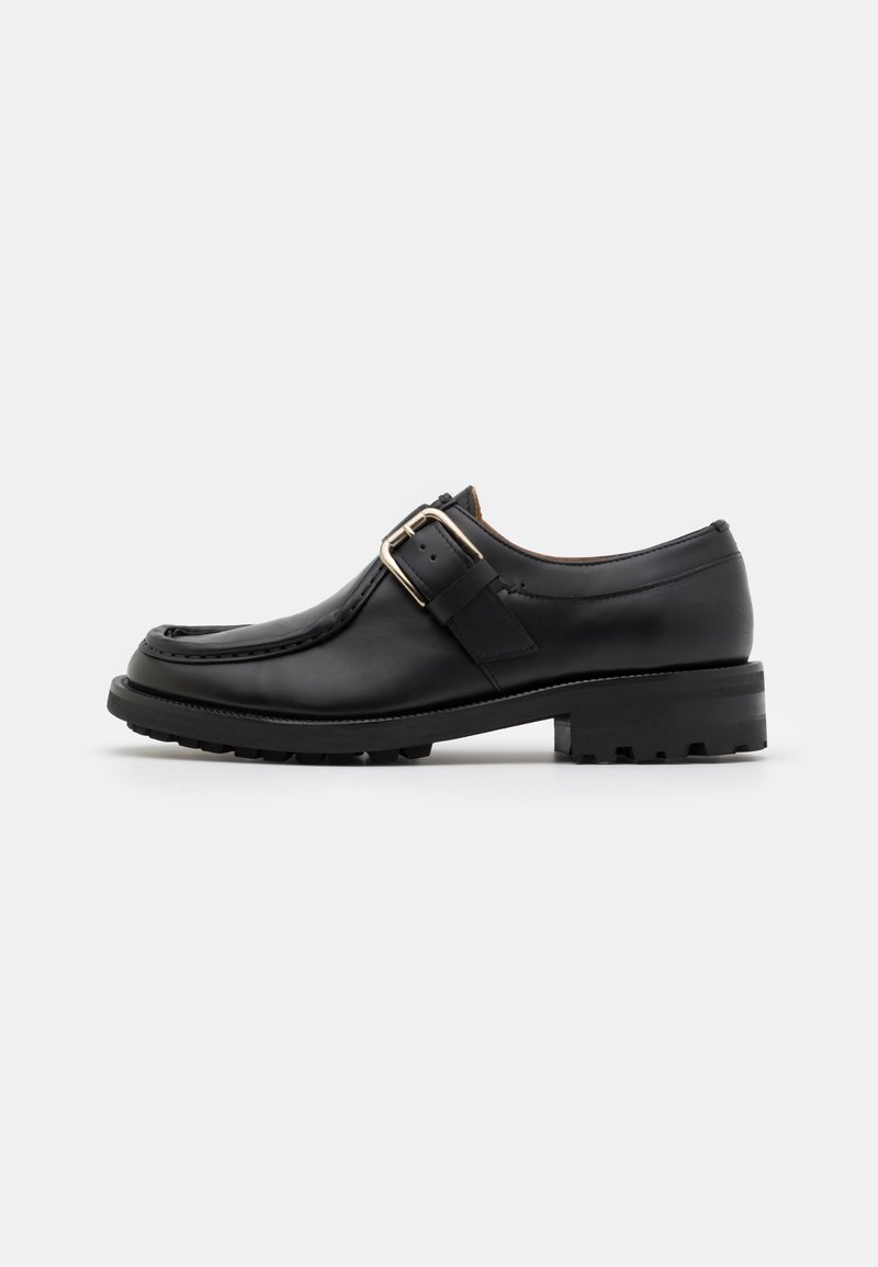 Black leather loafer with a silver buckle strap, chunky sole, and moc toe stitching, shown from the side on a plain white background.