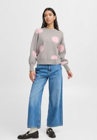 Grey sweater with large pink polka dots, relaxed fit, paired with wide-leg blue jeans and black loafers, showcasing a casual style.