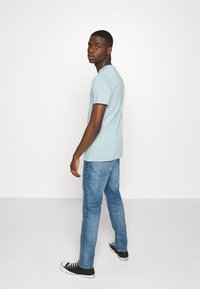 T-shirt azzurro a maniche corte, indossato con jeans in denim blu e sneakers nere. Il taglio è casual, con un semplice scollo tondo.