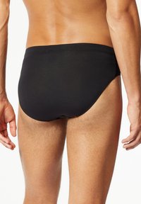 Costume da bagno neri con una vestibilità aderente, caratterizzati da una superficie liscia e un design minimalista; nessun marchio o dettaglio visibile.