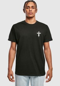 Sort bomulds T-shirt med rund udskæring, korte ærmer og et hvidt korsdesign på venstre bryst. Blød tekstur, afslappet pasform.