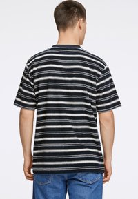 Camiseta de manga corta a rayas en blanco y negro con cuello redondo; tejido texturizado; corte holgado; vista trasera con detalles de costura visibles.